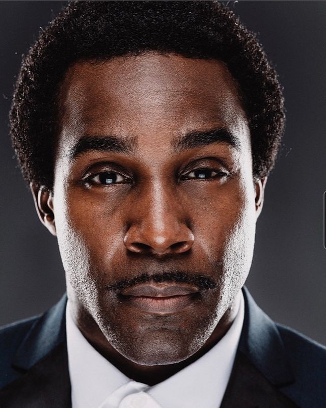 Tramell Tillman in a white shirt and black coat.